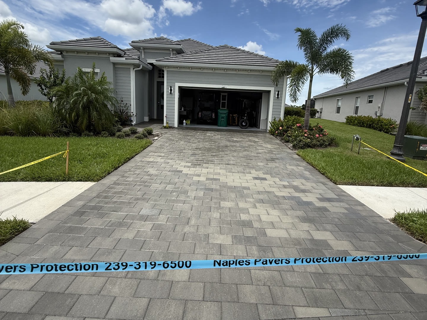 A Naples home with its paver driveway freshly cleaned and sealed, taped off while the sealer cures