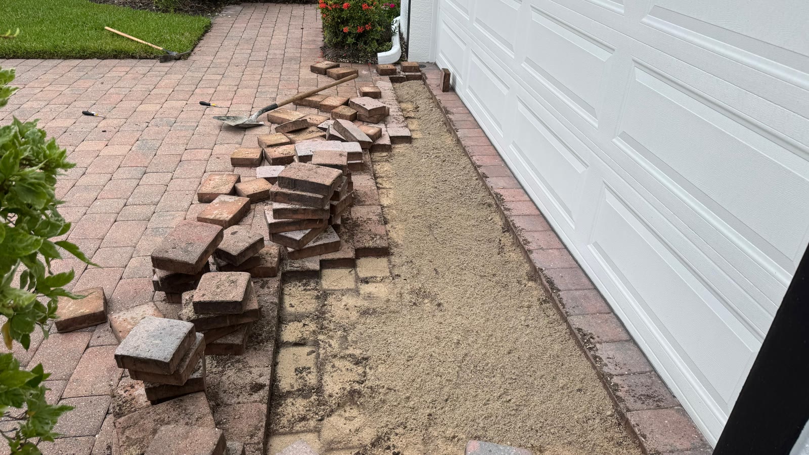 Pavers lifted off a Naples driveway with the sand base exposed and re-graded